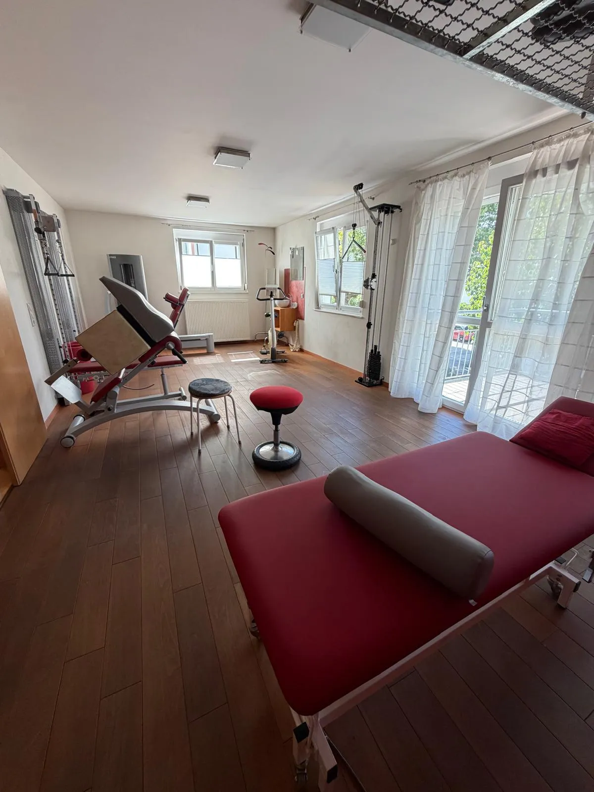 Trainings- und Behandlungsraum in Gengenbach mit Zugapparat, Trainingsbank und Tür zum Balkon.